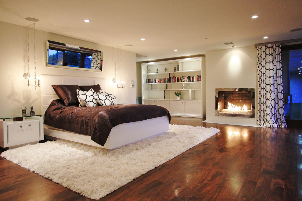 Пример оригинального дизайна: спальня в современном стиле с белыми стенами, темным паркетным полом и стандартным камином