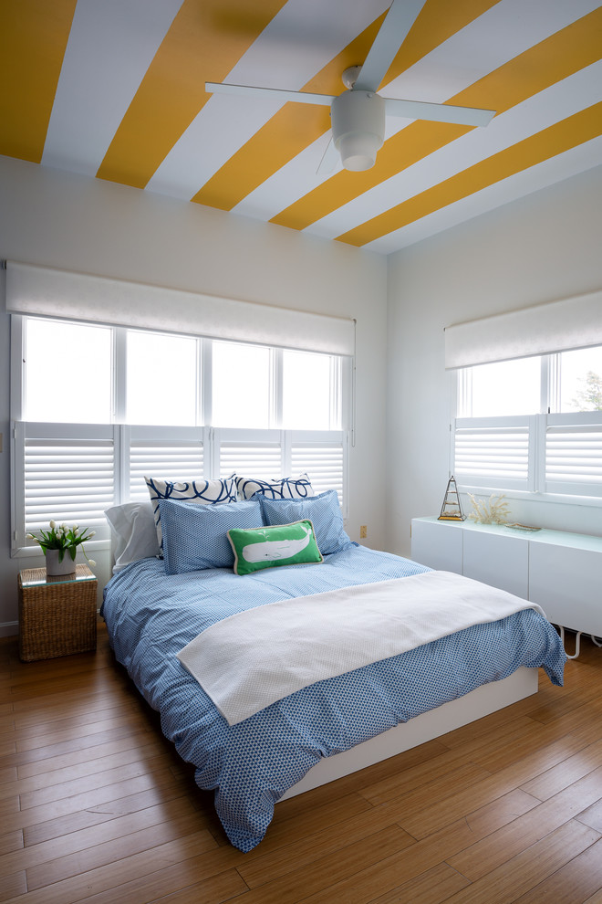 Diseño de habitación de invitados costera sin chimenea con paredes blancas y suelo de madera en tonos medios