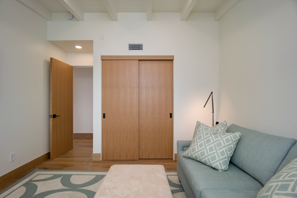 Modelo de habitación de invitados actual de tamaño medio con paredes blancas, suelo de madera clara, suelo beige y vigas vistas
