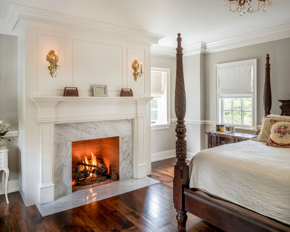 Klassisches Hauptschlafzimmer mit grauer Wandfarbe, braunem Holzboden, Kamin und Kaminumrandung aus Stein in Philadelphia