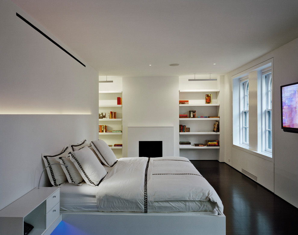 Immagine di una camera da letto moderna di medie dimensioni con pareti bianche, parquet scuro, camino classico, cornice del camino in intonaco e pavimento marrone