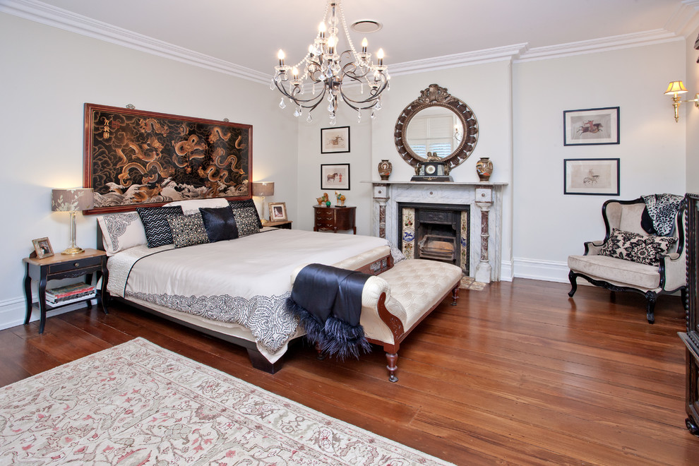 Cette photo montre une grande chambre parentale éclectique avec un mur blanc, un sol en bois brun, une cheminée standard et un manteau de cheminée en pierre.
