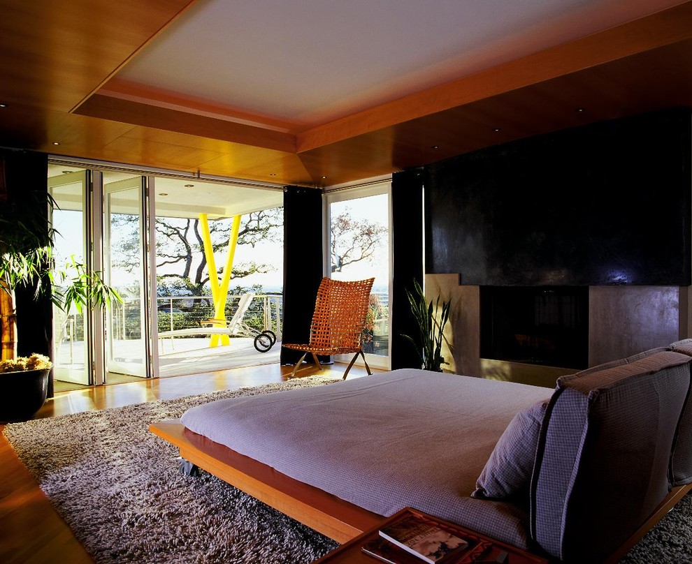 Immagine di una camera da letto stile loft con cornice del camino in cemento, pareti grigie, pavimento in legno massello medio e camino classico