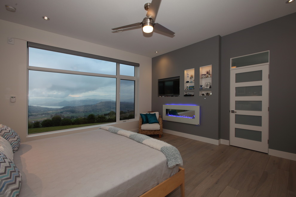 Foto de dormitorio principal moderno grande con paredes blancas, suelo de madera clara, chimenea lineal y marco de chimenea de yeso