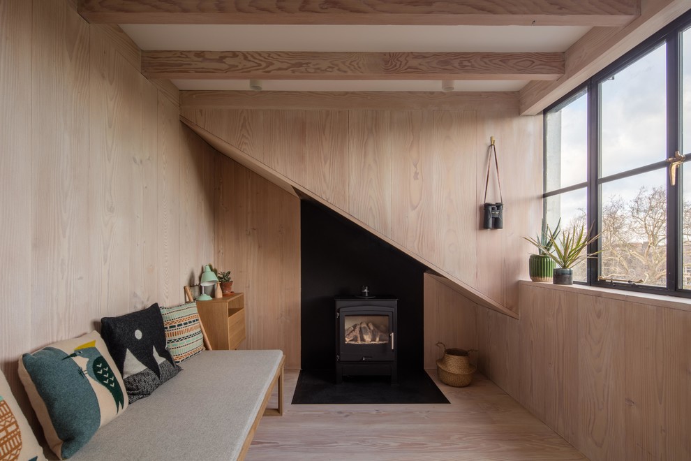 Bild på ett litet nordiskt gästrum, med ljust trägolv, en öppen vedspis, en spiselkrans i metall, bruna väggar och beiget golv