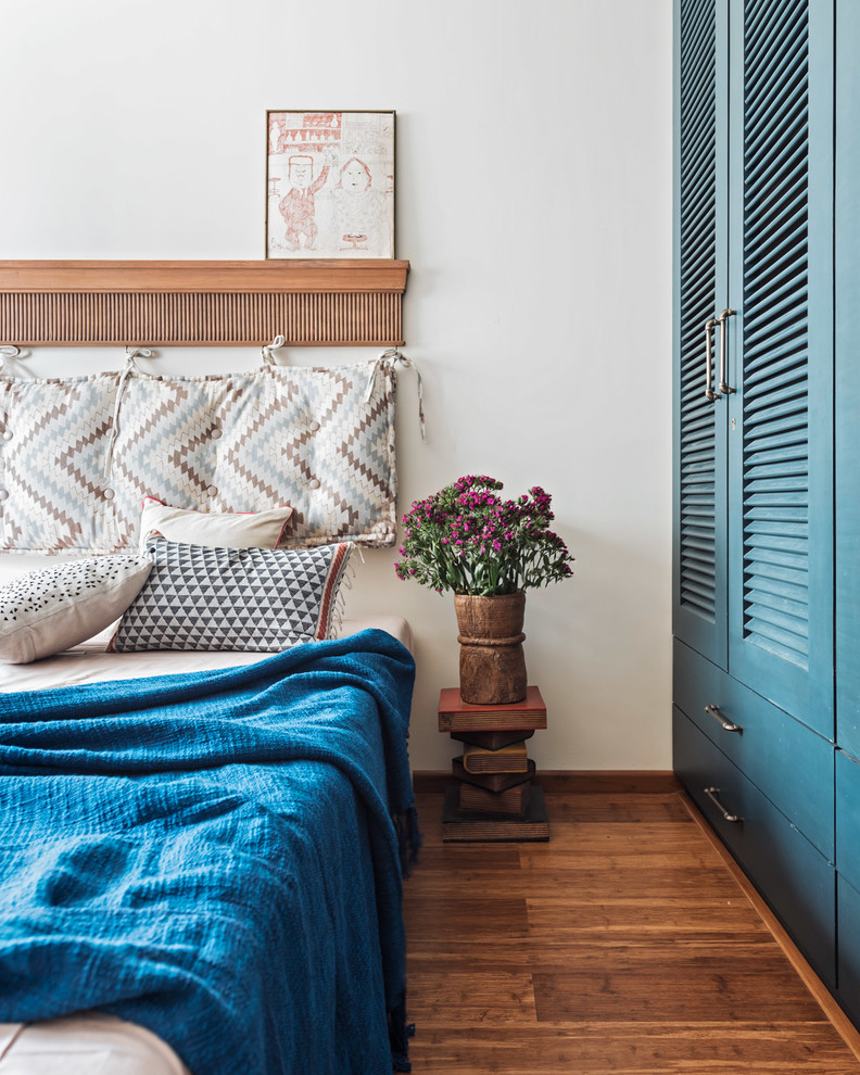 Eclectic bedroom in Mumbai with white walls, medium hardwood flooring and brown floors.