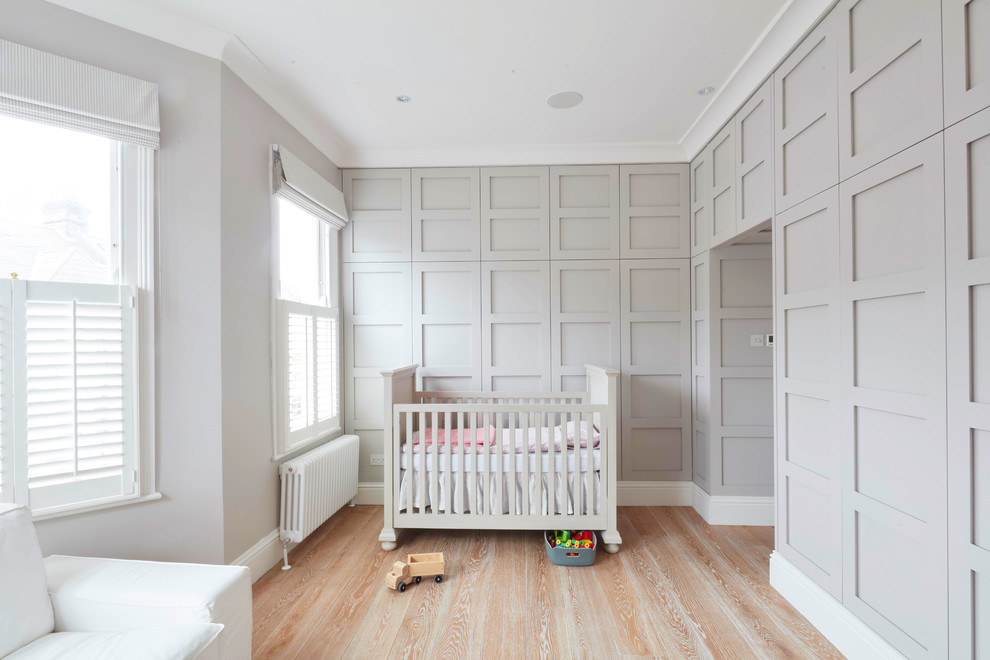 Modelo de habitación de bebé clásica grande con paredes grises y suelo de madera en tonos medios