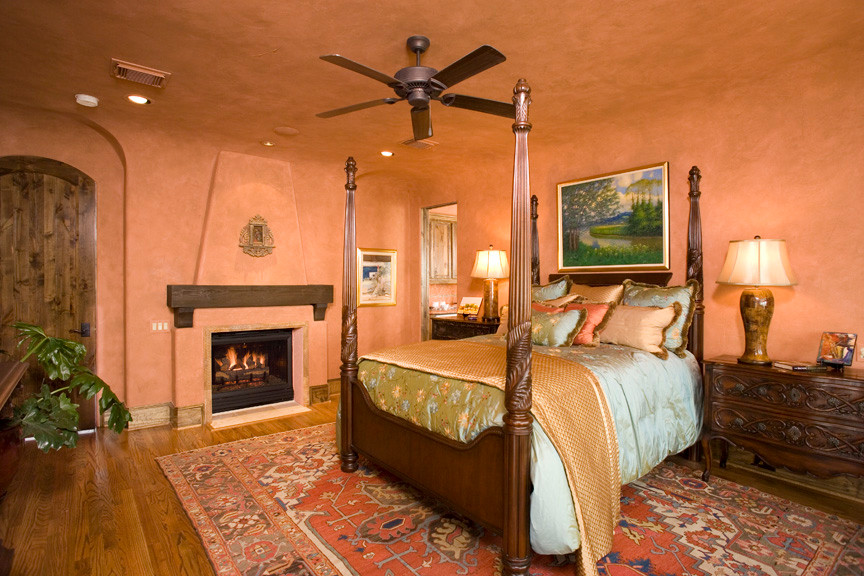 На фото: огромная хозяйская спальня в средиземноморском стиле с оранжевыми стенами, паркетным полом среднего тона, стандартным камином и фасадом камина из штукатурки