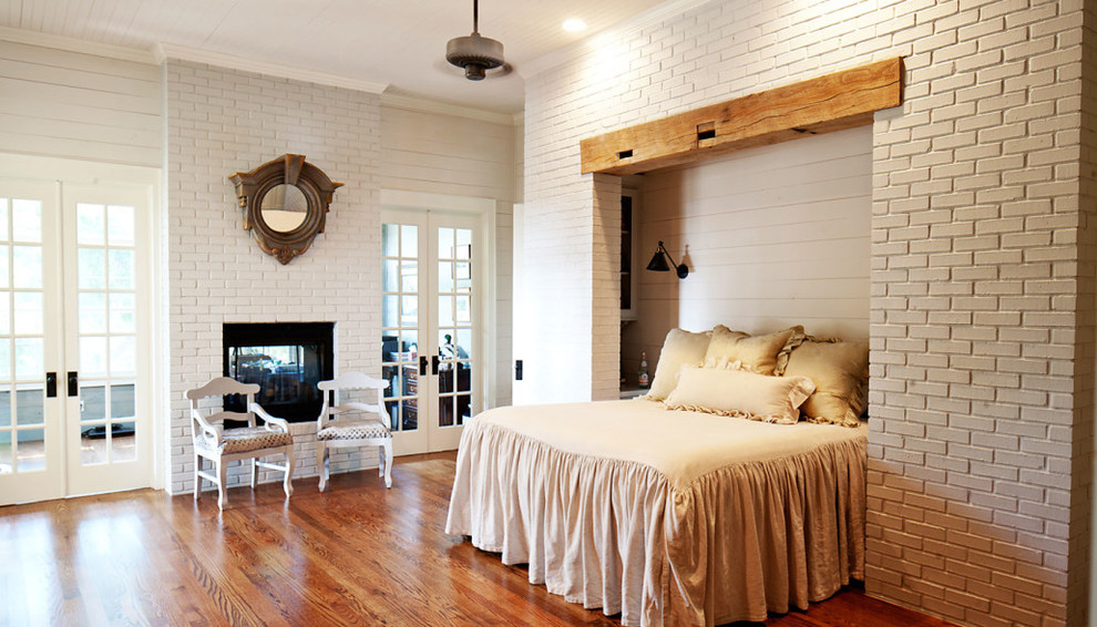 Réalisation d'une chambre parentale tradition de taille moyenne avec un mur blanc, un sol en bois brun, une cheminée double-face et un manteau de cheminée en brique.