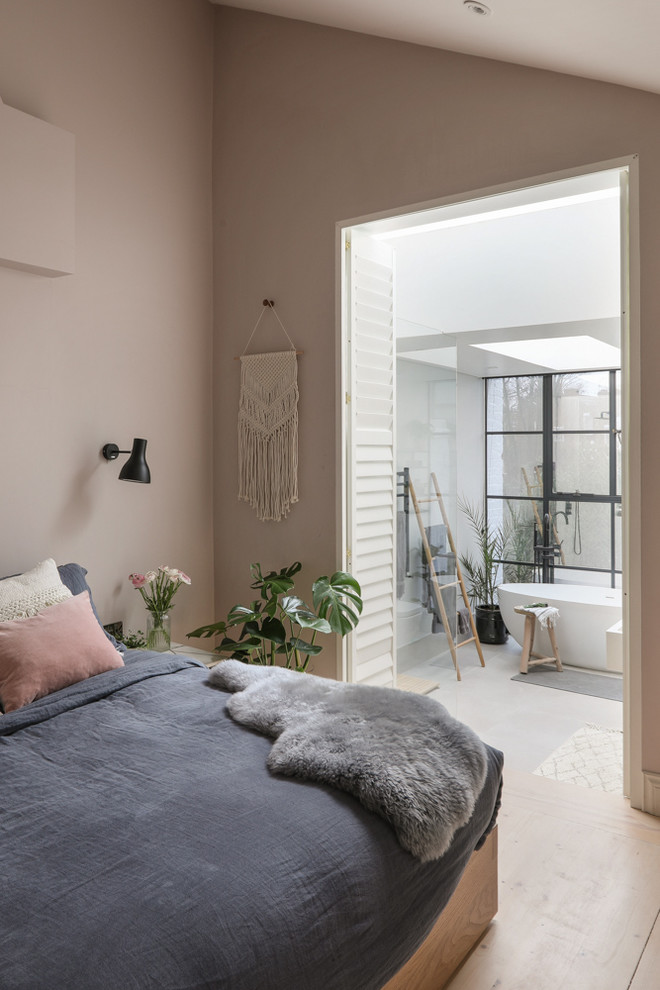 Photo of a large scandi master and grey and pink bedroom in London with pink walls and light hardwood flooring.