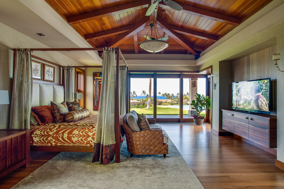 Immagine di una camera da letto tropicale con pareti beige, pavimento in legno massello medio e TV