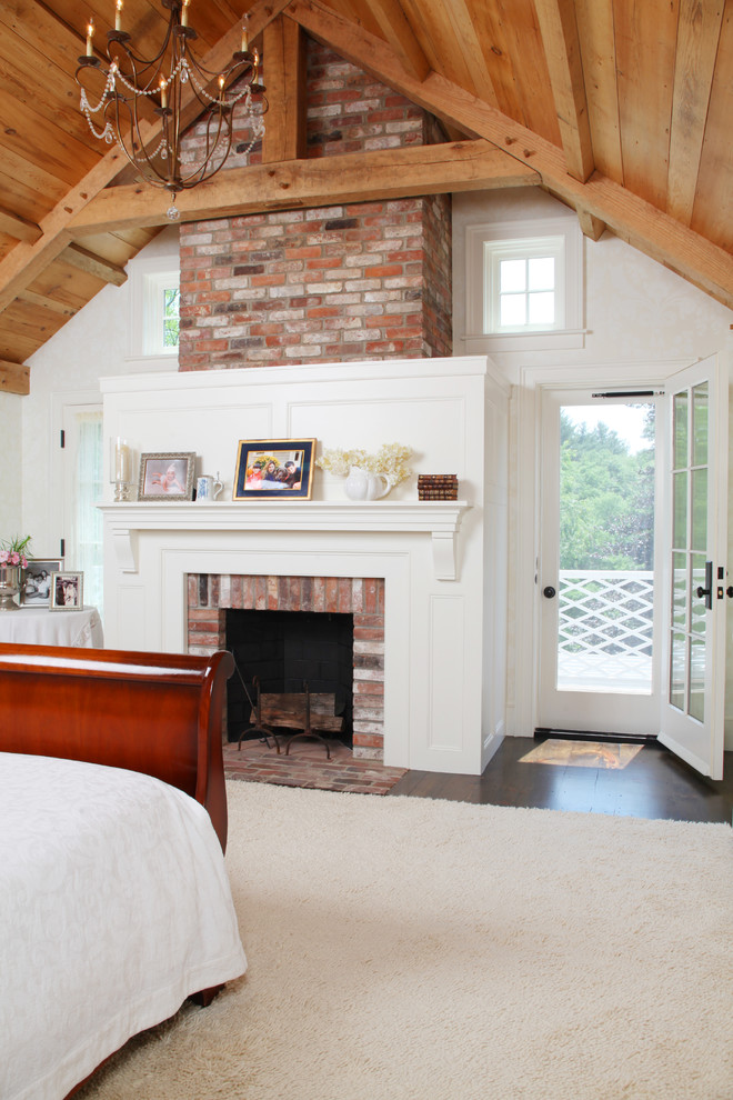 Réalisation d'une grande chambre parentale champêtre avec un mur blanc, parquet foncé, une cheminée standard, un manteau de cheminée en brique et un sol marron.