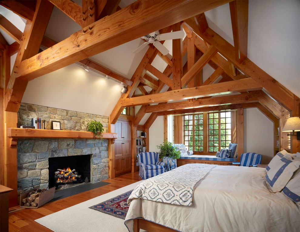 Imagen de dormitorio principal tradicional de tamaño medio con paredes blancas, todas las chimeneas, marco de chimenea de piedra y suelo de madera en tonos medios