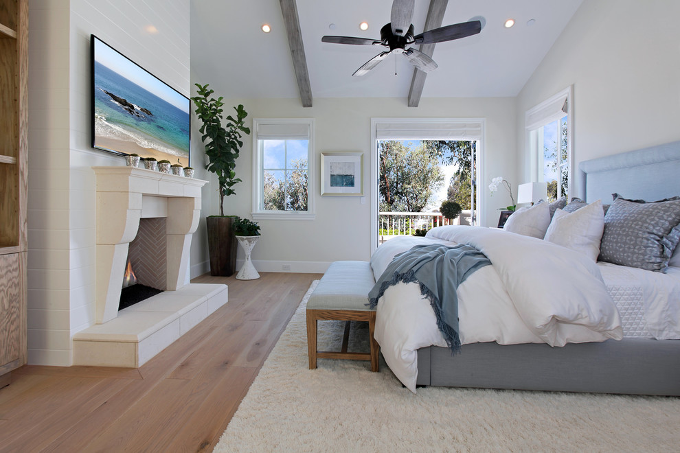 Maritimes Schlafzimmer mit weißer Wandfarbe, braunem Holzboden und Kamin in Orange County