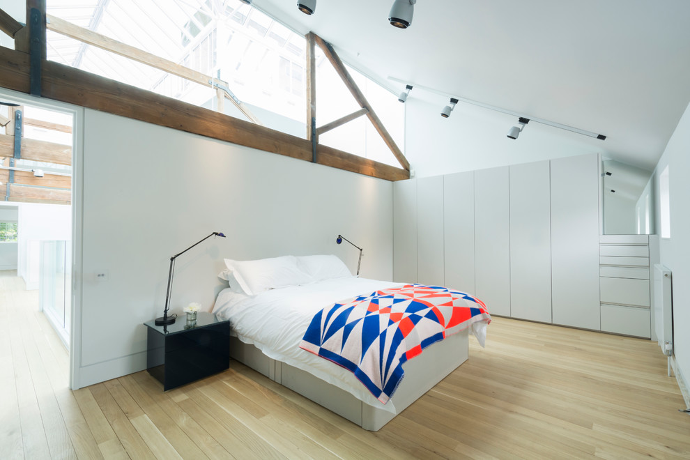 Inspiration for an expansive urban master bedroom in London with white walls and light hardwood flooring.