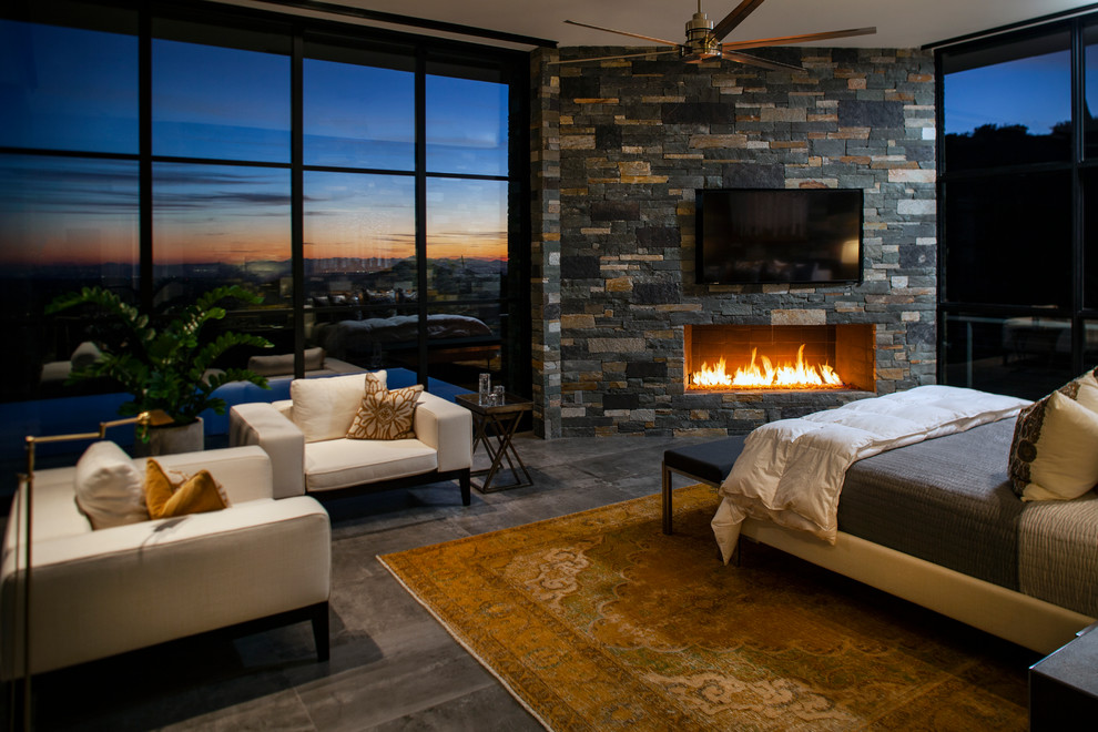 Expansive contemporary master bedroom in Phoenix with white walls, porcelain flooring, a standard fireplace, a stone fireplace surround and grey floors.