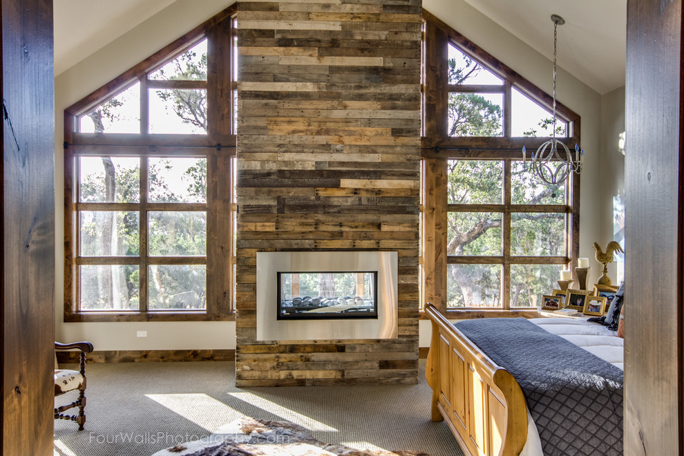 Photo of an expansive rustic master bedroom in Austin with white walls, carpet, a two-sided fireplace and a wooden fireplace surround.