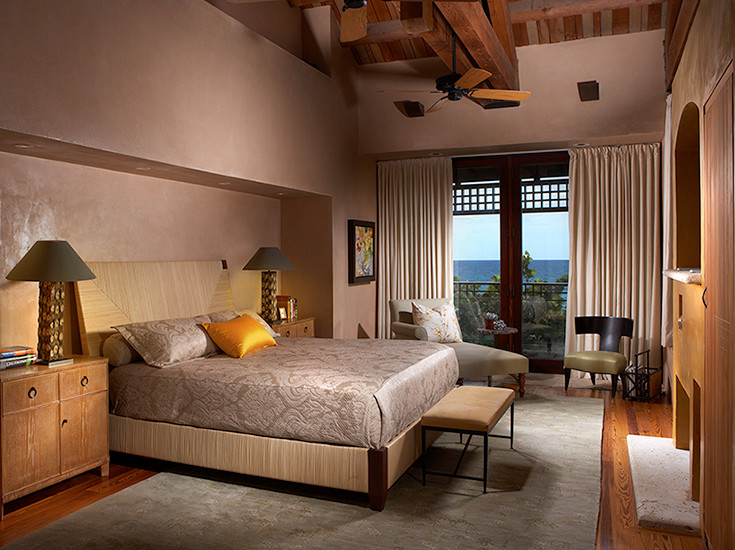 Modelo de dormitorio principal moderno grande con paredes beige, suelo de madera en tonos medios, todas las chimeneas y marco de chimenea de yeso