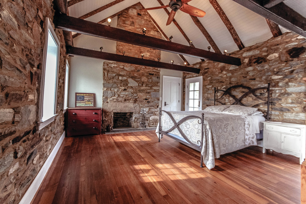 Diseño de dormitorio principal campestre de tamaño medio con suelo de madera clara, todas las chimeneas y marco de chimenea de piedra
