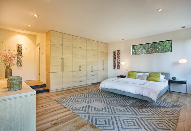 Cette image montre une grande chambre parentale minimaliste avec un mur blanc et un sol en bois brun.