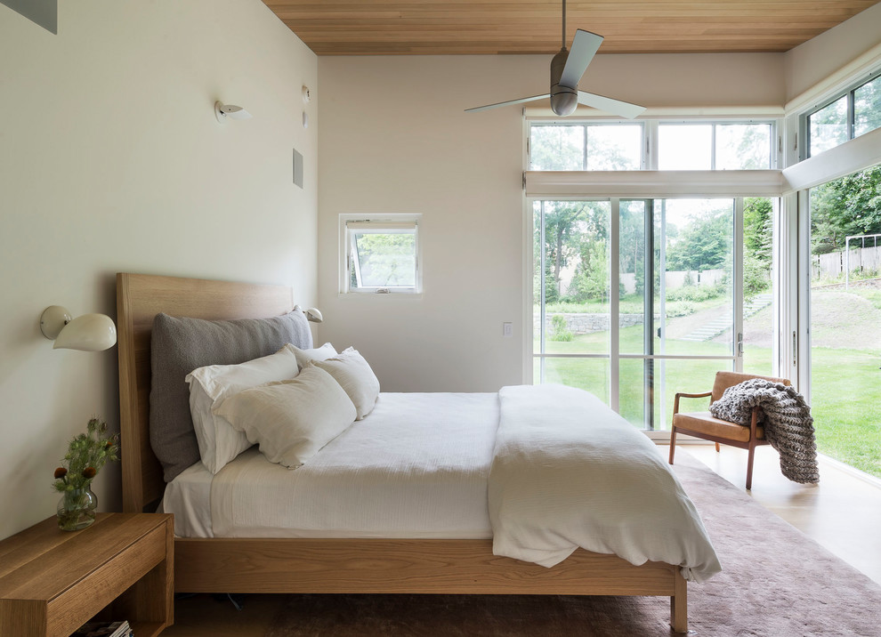 Modelo de dormitorio contemporáneo con paredes blancas, suelo de madera en tonos medios y suelo marrón