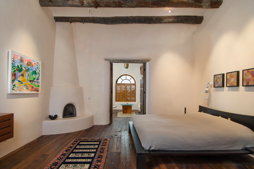 アルバカーキにある広いサンタフェスタイルのおしゃれな主寝室 (白い壁、無垢フローリング、コーナー設置型暖炉、漆喰の暖炉まわり)
