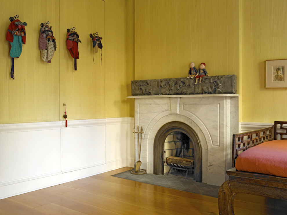 Modelo de habitación de invitados tradicional renovada de tamaño medio con paredes amarillas, suelo de madera en tonos medios, todas las chimeneas y marco de chimenea de piedra