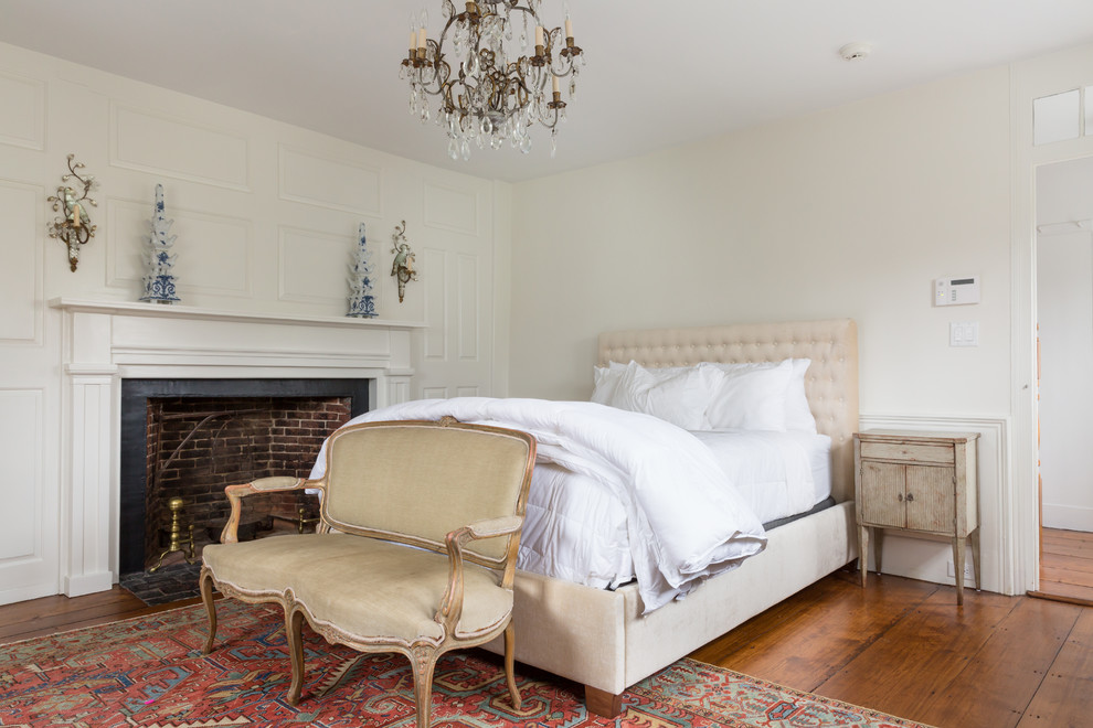 Photo of a farmhouse master bedroom in Boston with beige walls, medium hardwood flooring, a standard fireplace, a brick fireplace surround and brown floors.