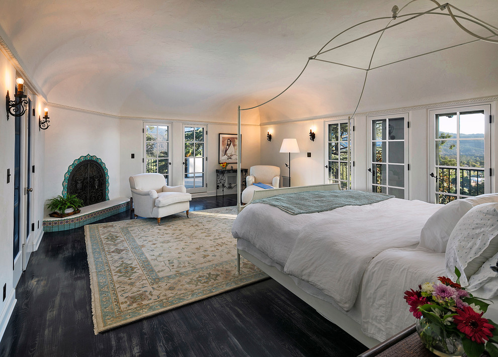 Großes Mediterranes Hauptschlafzimmer mit weißer Wandfarbe, gebeiztem Holzboden, Eckkamin und gefliester Kaminumrandung in Los Angeles