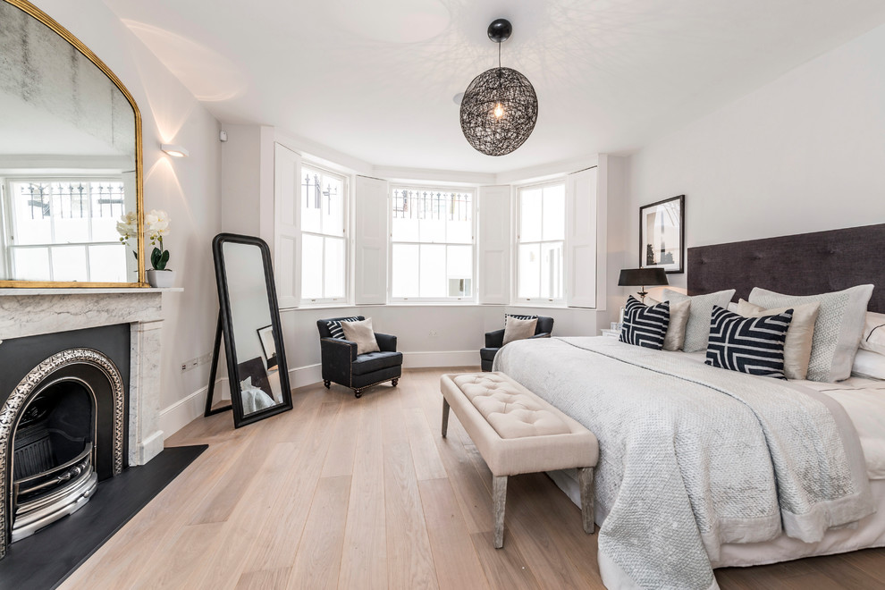 Inspiration for a classic cream and black bedroom in London with white walls, light hardwood flooring, a standard fireplace and beige floors.