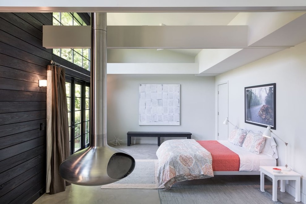 На фото: гостевая спальня среднего размера, (комната для гостей) в стиле модернизм с белыми стенами, бетонным полом, подвесным камином, фасадом камина из металла и серым полом