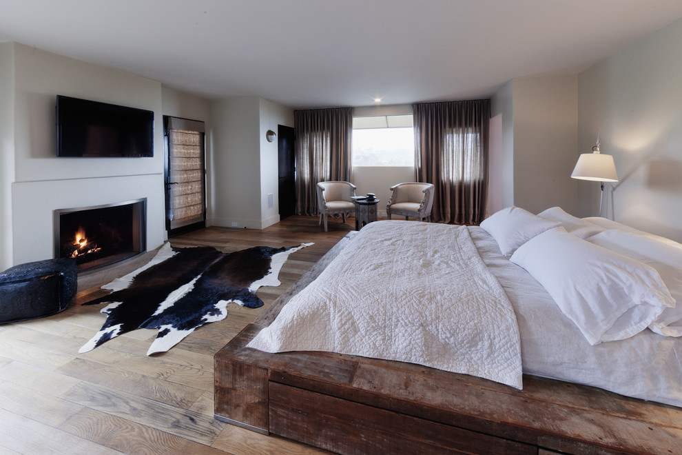 Ejemplo de dormitorio principal y televisión rústico con paredes grises, suelo de madera clara y todas las chimeneas