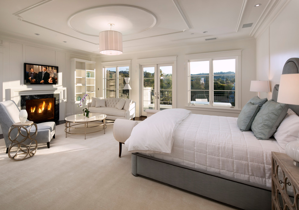 Geräumiges Klassisches Hauptschlafzimmer mit weißer Wandfarbe, Teppichboden, Kamin, Kaminumrandung aus Stein und weißem Boden in Los Angeles
