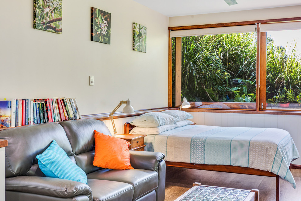 Modelo de dormitorio tropical con paredes blancas, suelo de madera en tonos medios y suelo marrón