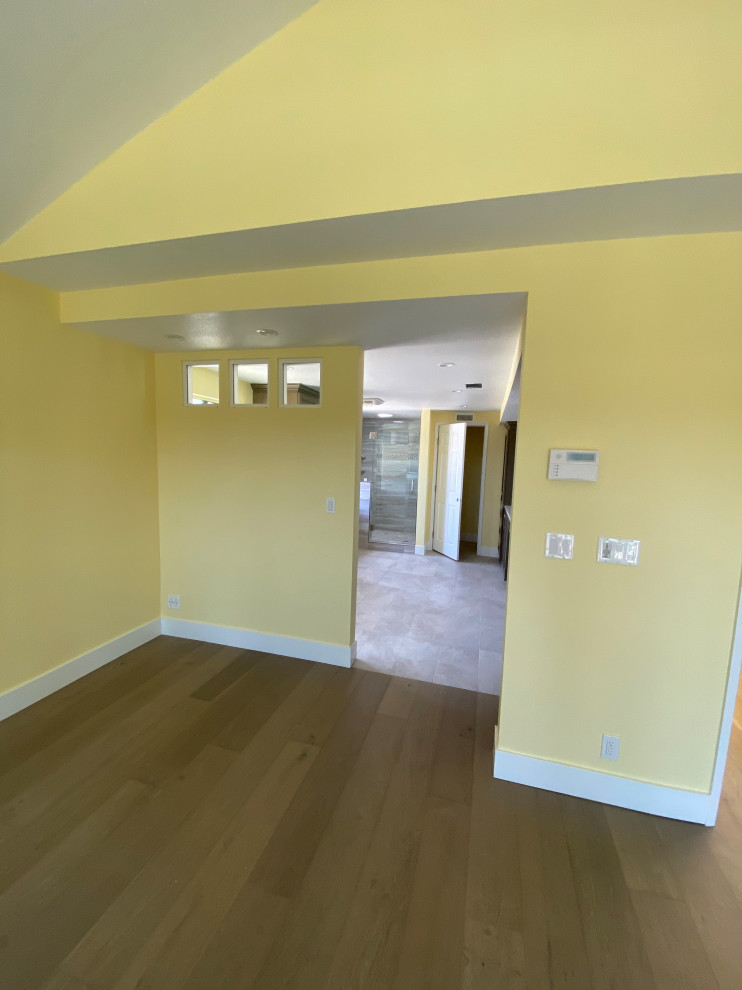 オレンジカウンティにある広いコンテンポラリースタイルのおしゃれな客用寝室 (黄色い壁、淡色無垢フローリング、暖炉なし、茶色い床)