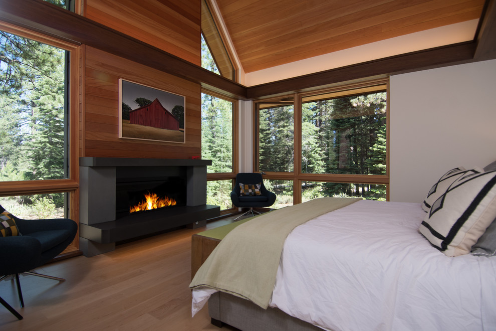 Ejemplo de dormitorio principal rústico de tamaño medio con paredes blancas, suelo de madera clara, chimenea lineal, marco de chimenea de hormigón y suelo beige