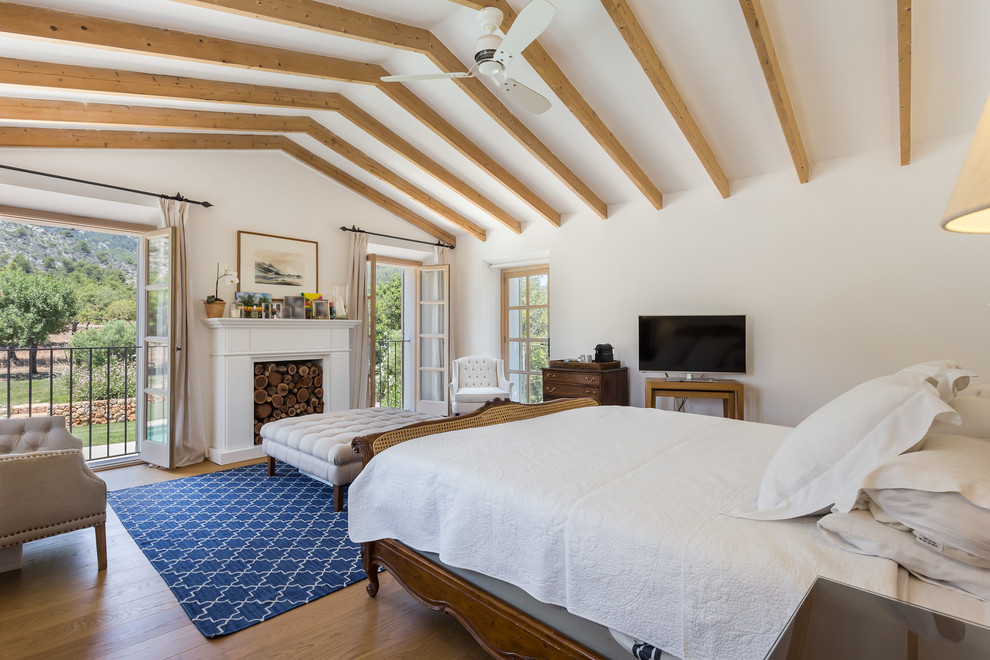 Imagen de dormitorio principal mediterráneo con paredes blancas, suelo de madera en tonos medios, todas las chimeneas y suelo marrón