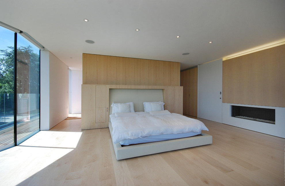 Ejemplo de dormitorio principal actual grande con paredes blancas, suelo de madera clara y chimenea lineal