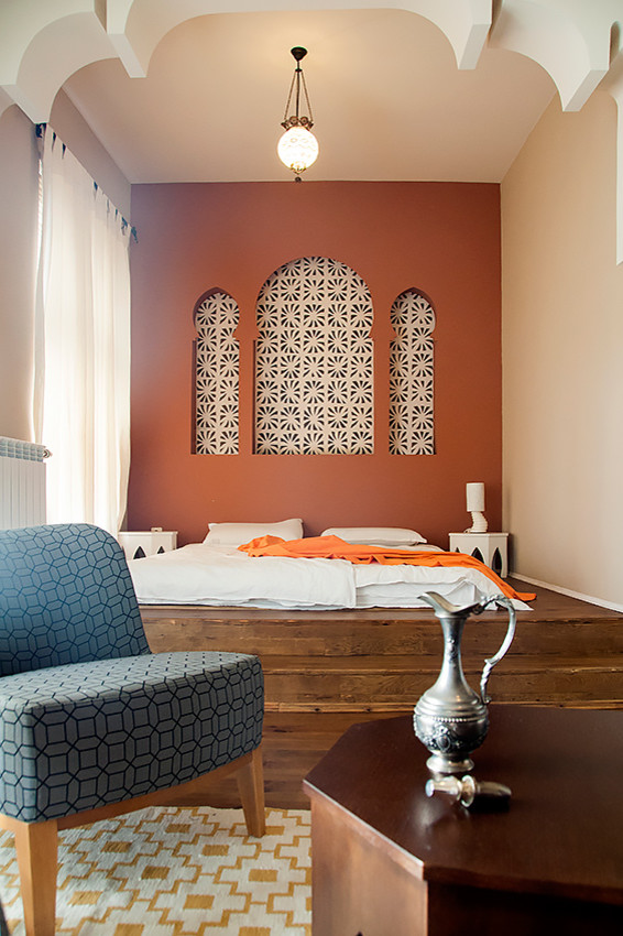 Medium sized world-inspired master bedroom in Other with orange walls and light hardwood flooring.