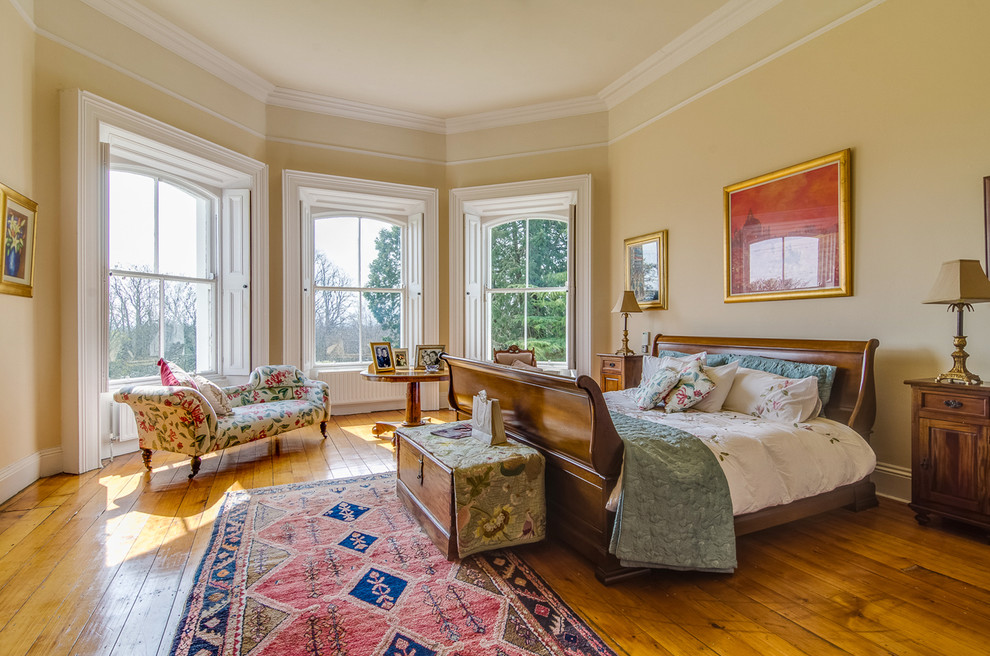 Modelo de dormitorio principal clásico sin chimenea con paredes amarillas y suelo de madera en tonos medios