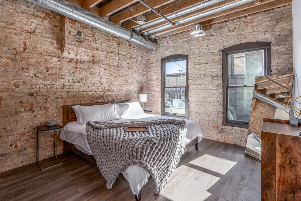 Ejemplo de dormitorio industrial de tamaño medio sin chimenea con suelo marrón, ladrillo y vigas vistas