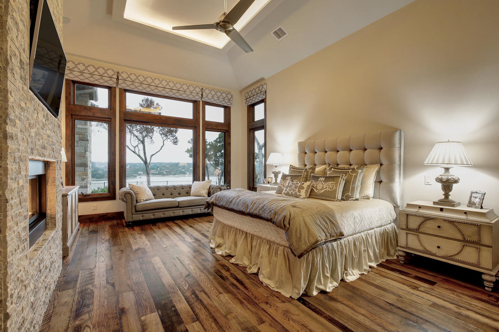 Geräumiges Klassisches Hauptschlafzimmer mit weißer Wandfarbe, hellem Holzboden, Kaminumrandung aus Stein, Gaskamin und buntem Boden in Austin