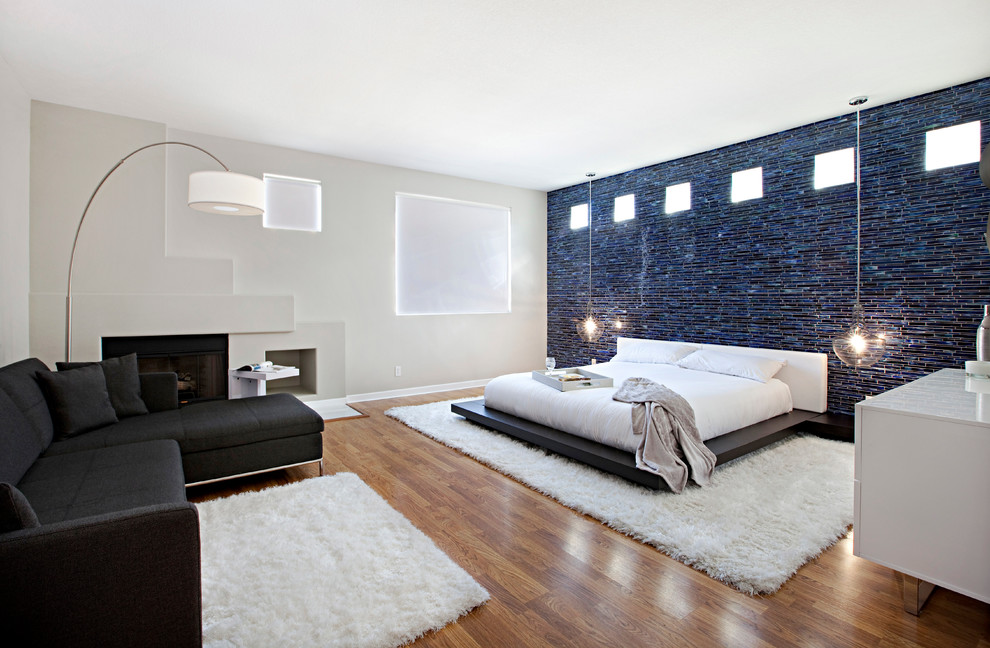 Modelo de dormitorio principal contemporáneo de tamaño medio con paredes grises, suelo de madera clara, todas las chimeneas y marco de chimenea de metal