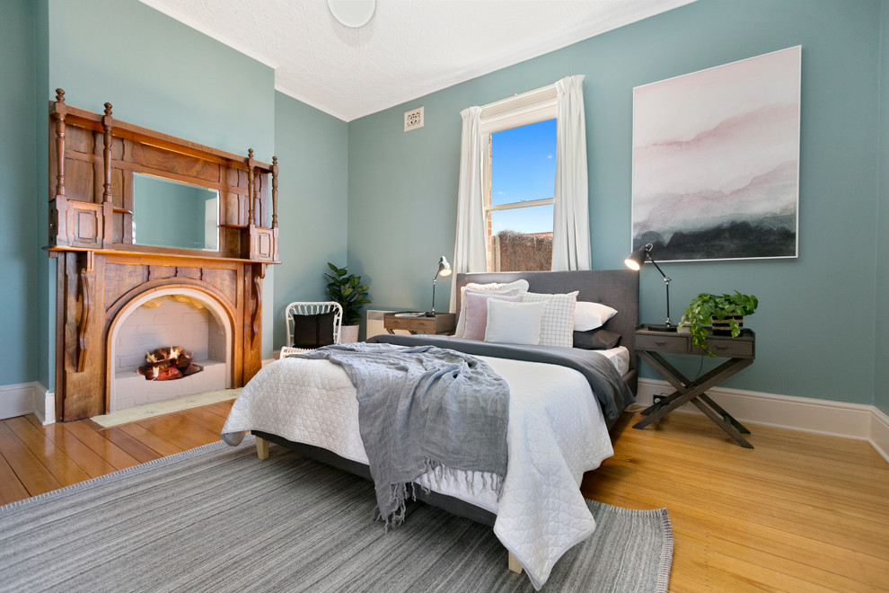 ホバートにあるトランジショナルスタイルのおしゃれな寝室 (青い壁、無垢フローリング、標準型暖炉、木材の暖炉まわり、茶色い床) のレイアウト