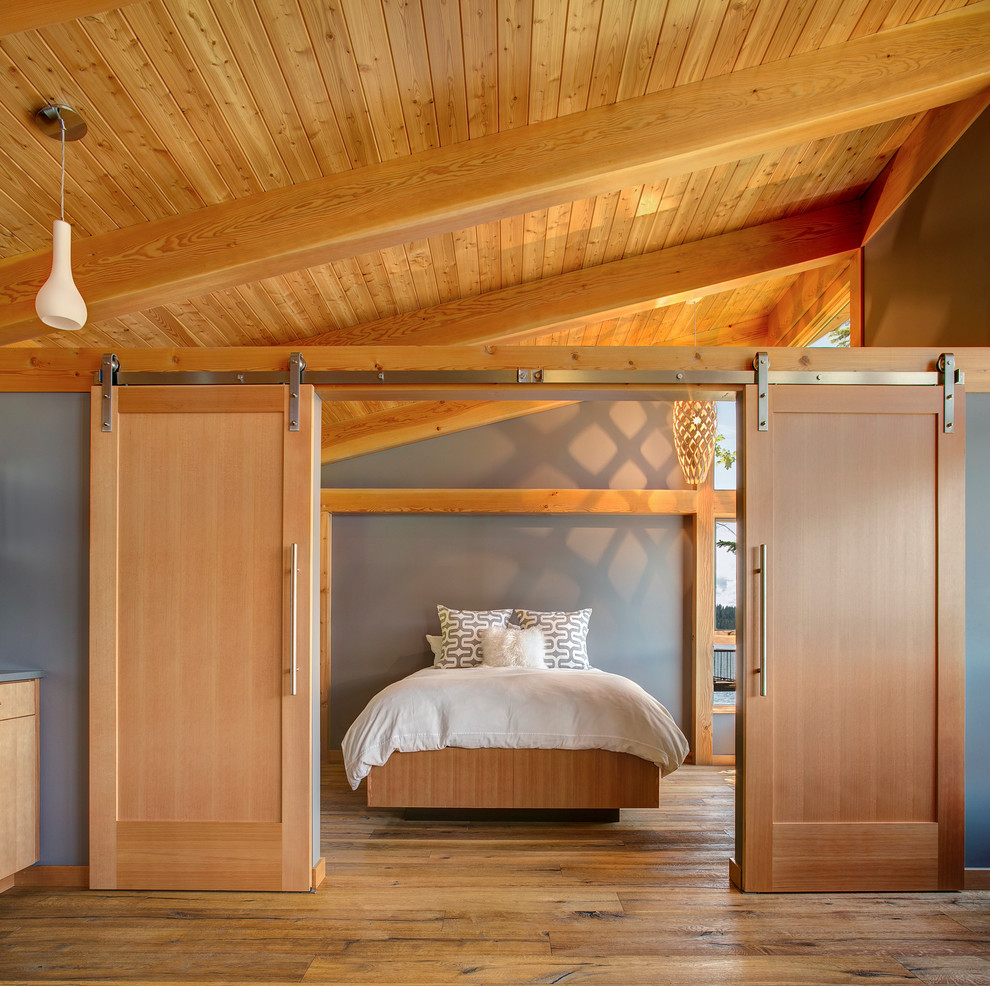 Diseño de dormitorio principal rural grande sin chimenea con paredes grises, suelo de madera en tonos medios y suelo marrón