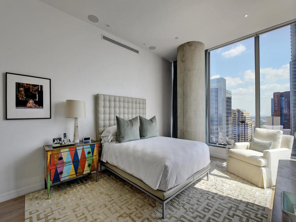 This is an example of an urban master bedroom in Austin with white walls, no fireplace and medium hardwood flooring.