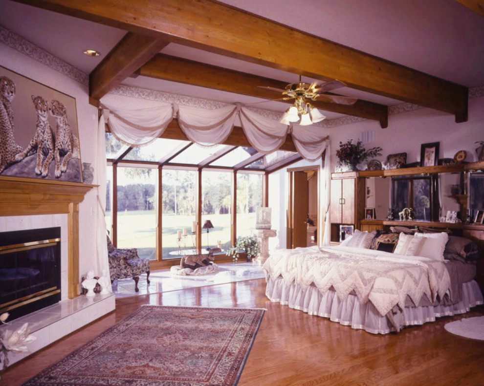 На фото: большая хозяйская спальня с белыми стенами, паркетным полом среднего тона, стандартным камином и фасадом камина из дерева