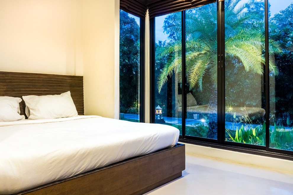 Imagen de dormitorio principal tropical de tamaño medio sin chimenea con paredes amarillas, suelo de cemento y suelo gris