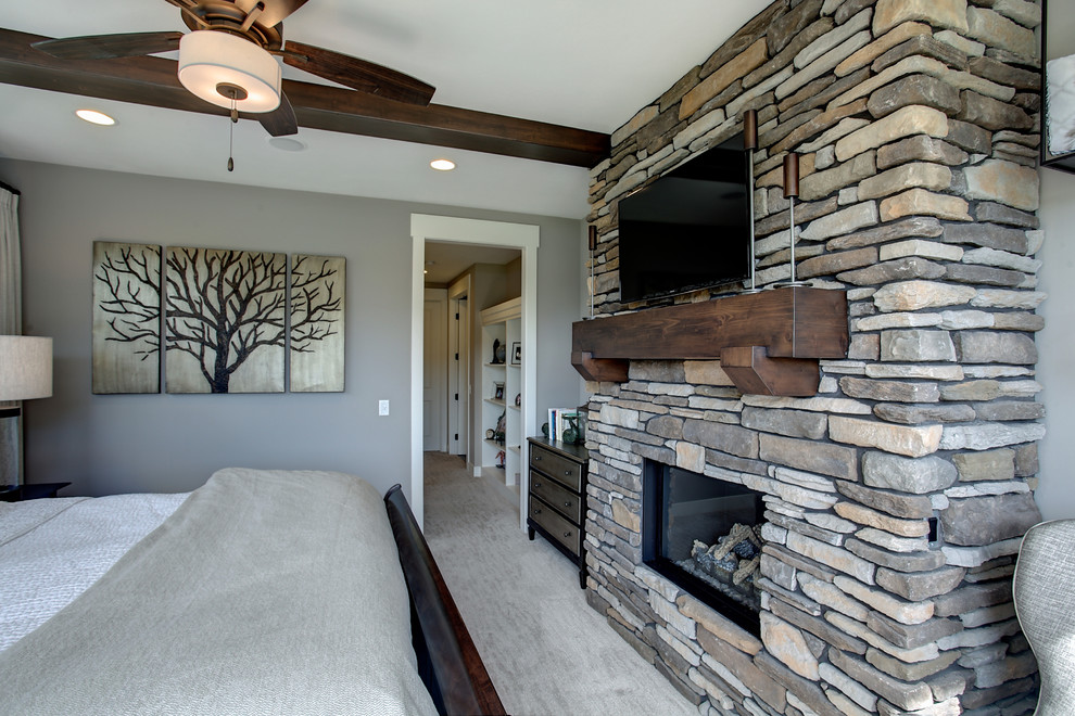 Medium sized rustic master bedroom in Grand Rapids with beige walls, carpet, a standard fireplace, a stone fireplace surround and beige floors.