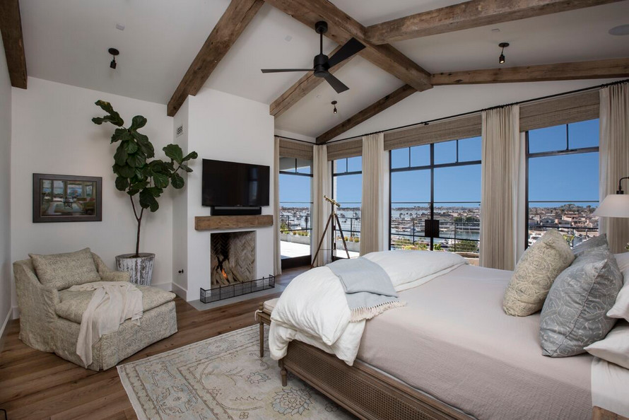 Großes Mediterranes Hauptschlafzimmer mit weißer Wandfarbe, braunem Holzboden, Kamin und verputzter Kaminumrandung in Orange County